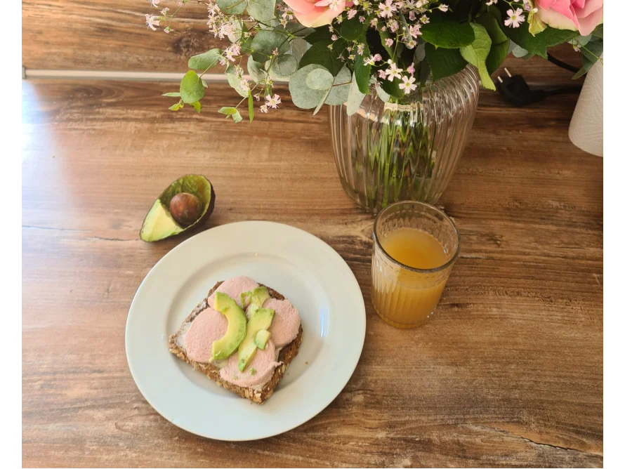 Ein belegtes Brot mit Avocado, ein Glas Saft und Blumen.