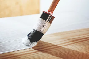Pinsel streicht weiße Farbe auf Holz