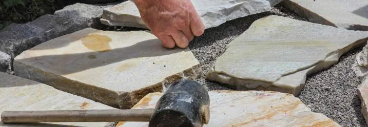 Person verlegt Steinplatten mit Gummihammer