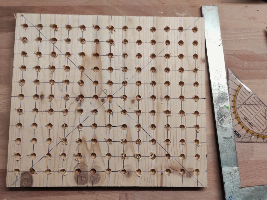 Lochplatte aus Holz mit Bleistiftmarkierungen und einem Anschlagwinkel
