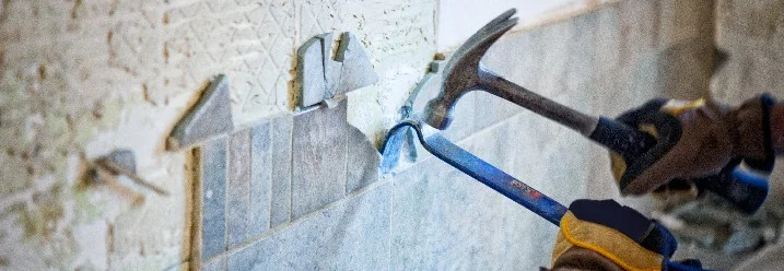 Person entfernt Fliesen mit Hammer und Meißel.