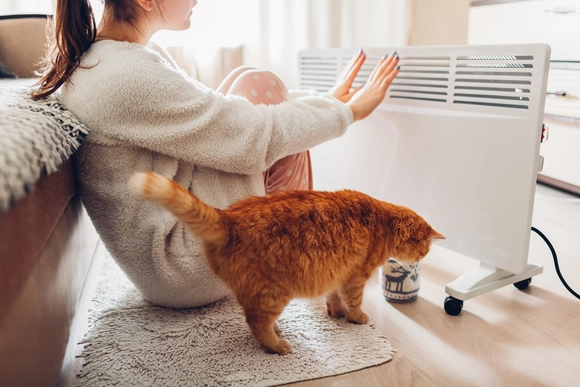 Person wärmt sich an mobiler Heizung, Katze sitzt daneben