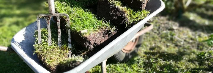 Schubkarre mit Grassoden und Heugabel