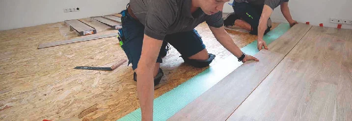 Zwei Personen verlegen Laminat auf Trittschalldämmung.