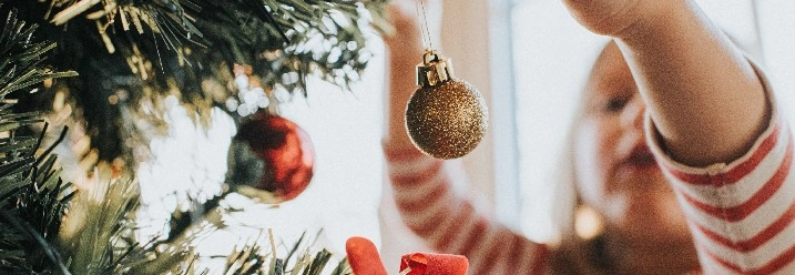 Ein Kind schmückt einen Weihnachtsbaum mit einer goldenen Christbaumkugel.