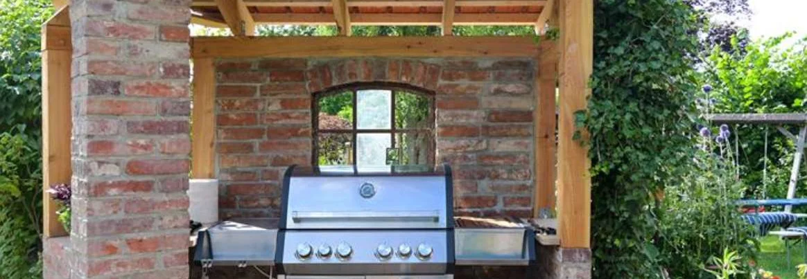 Moderner Stahlgasgrill in einem Unterstand aus alten Ziegeln und Holzkonzept-