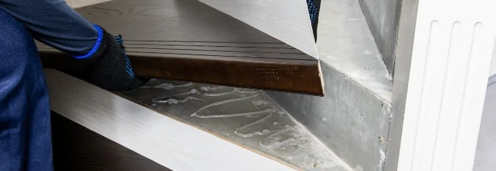 Eine Person montiert eine neue Holzstufe auf einer Betontreppe.