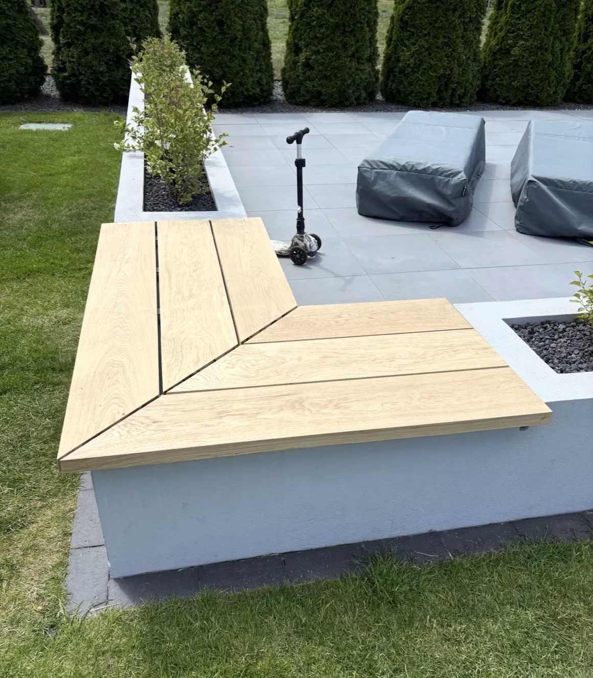 Eine L-förmige Holzbank auf einer grauen Gartenmauer.