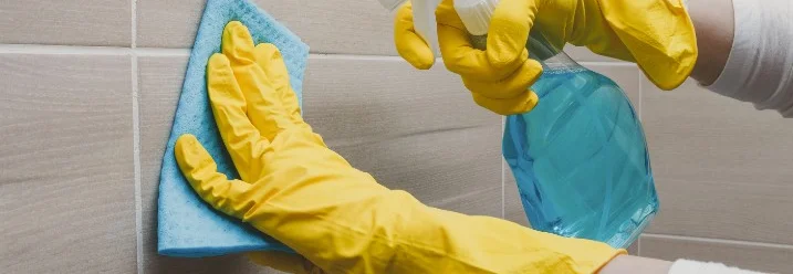 Person reinigt Fliesen mit Spray