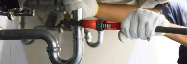 Person repariert Siphon mit Rohrzange.