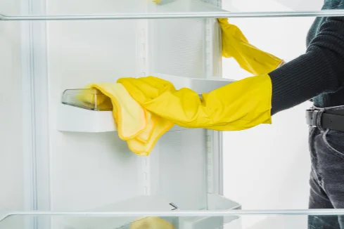 Person reinigt Kühlschrank mit Tuch.