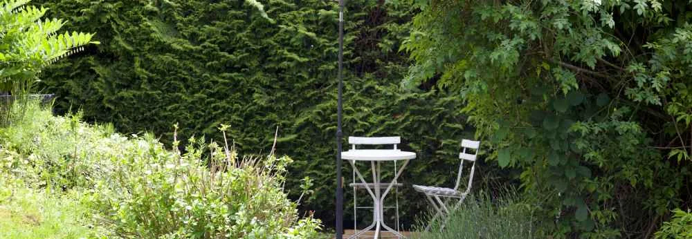 Eine kleine weiße Sitzgruppe mit Sonnenschirm steht in einem üppig grünen Garten.