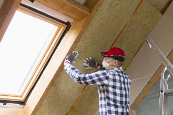 Eine Person bringt Dämmung an einer Dachschräge neben einem Dachfenster an.