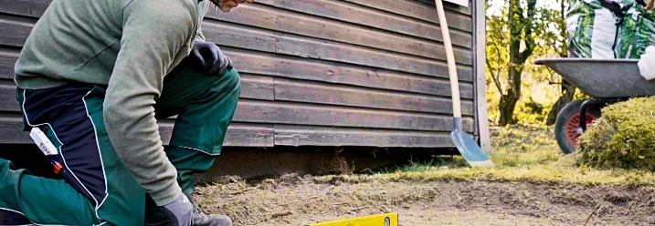 Person verwendet eine Wasserwaage auf Untergrund im Garten