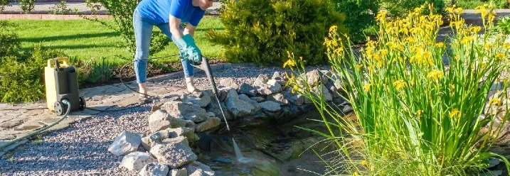 Person reinigt Teich mit Hochdruckreiniger