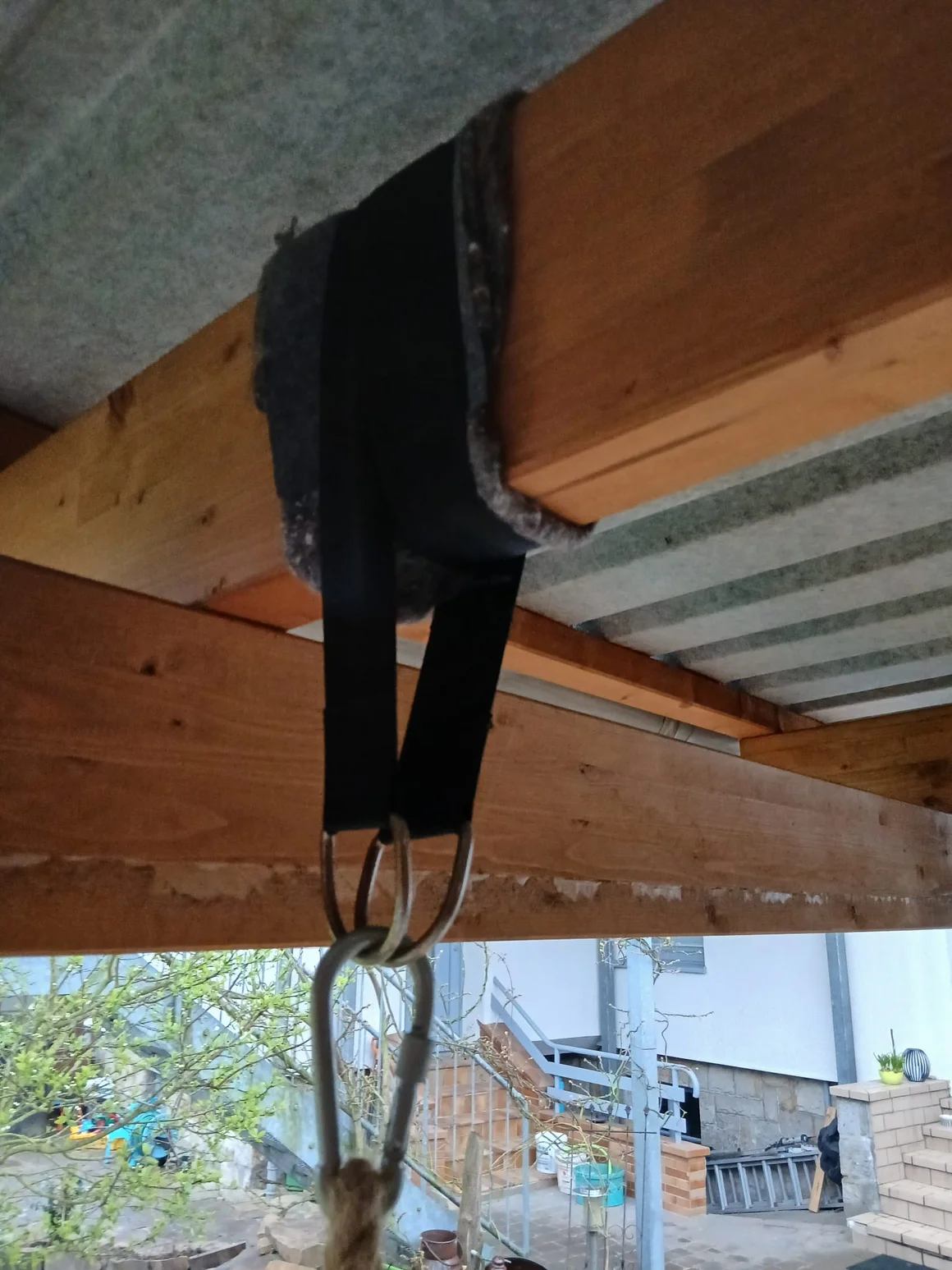 Aufhängung mit Gurt und Karabiner an einem Holzbalken.