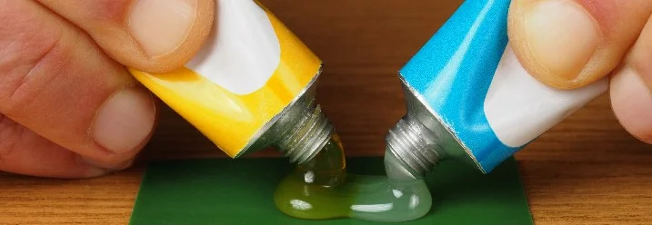Zwei Tuben Kleber werden auf eine Fläche gedrückt.
