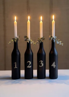 Vier schwarze, nummerierte Flaschen mit brennenden Kerzen als moderner Adventskranz.