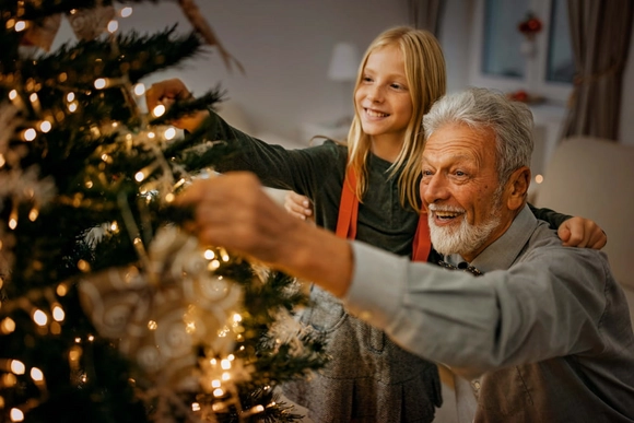 Ein älterer Mensch und ein Kind schmücken zusammen einen leuchtenden Weihnachtsbaum.