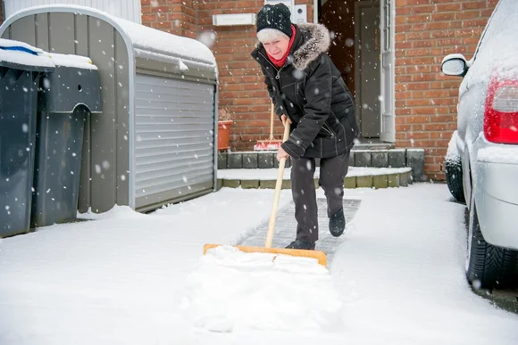 Person räumt Schnee mit Schneeschieber