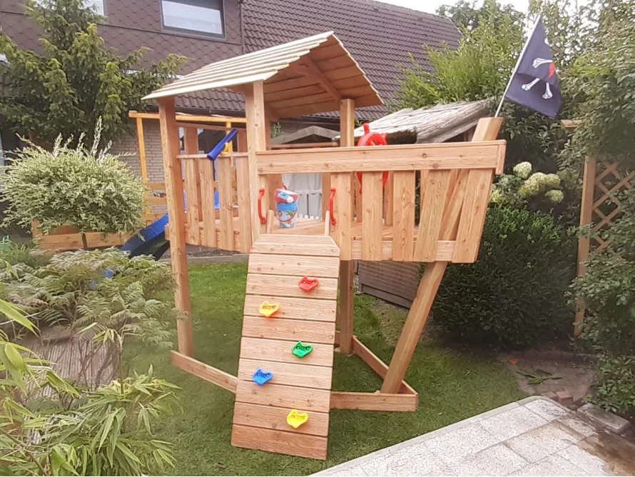 Hölzernes Spielgerät in Form eines Piratenschiffs mit Rutsche und Kletterwand.