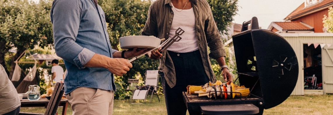 Zwei Personen grillen mit einer Grillzange Gemüse.