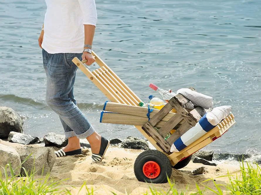 Person zieht Bollerwagen mit Strandutensilien