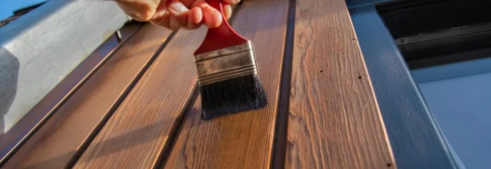Eine Holzfassade wird mit einem Pinsel gestrichen