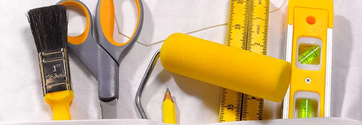 Verschiedene Malerwerkzeuge wie Pinsel und Farbroller in der Tasche eines weißen Kittels.