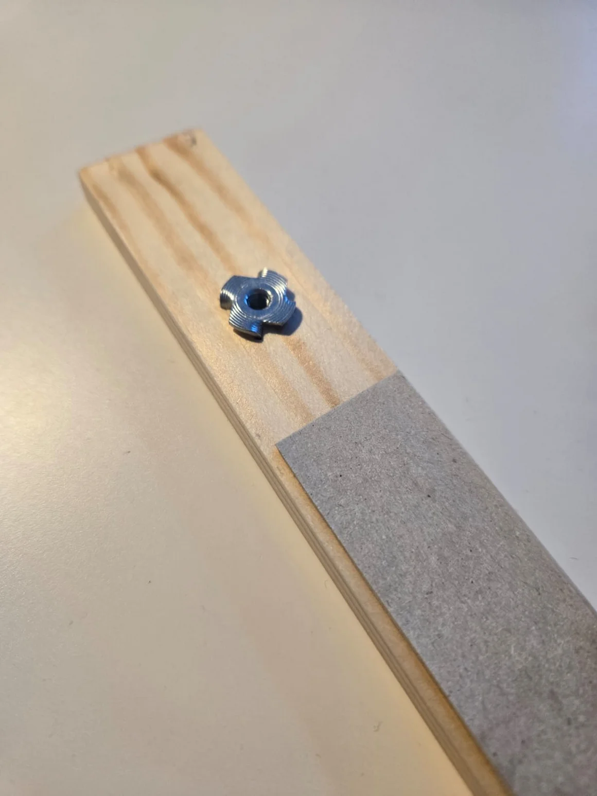 Eine Einschlagmutter auf einer Holzleiste neben einem Streifen Schleifpapier.