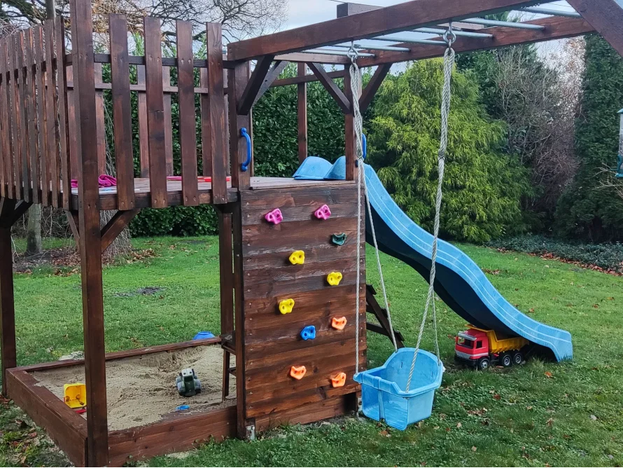 Ein Spielplatz aus Holz mit Rutsche, Schaukel und Kletterwand.