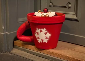 Rote Tasse mit Schneeflocke und Weihnachtskugeln als Dekoration.