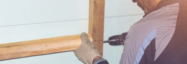 Person montiert Holzbalken mit Akkuschrauber an Wand.