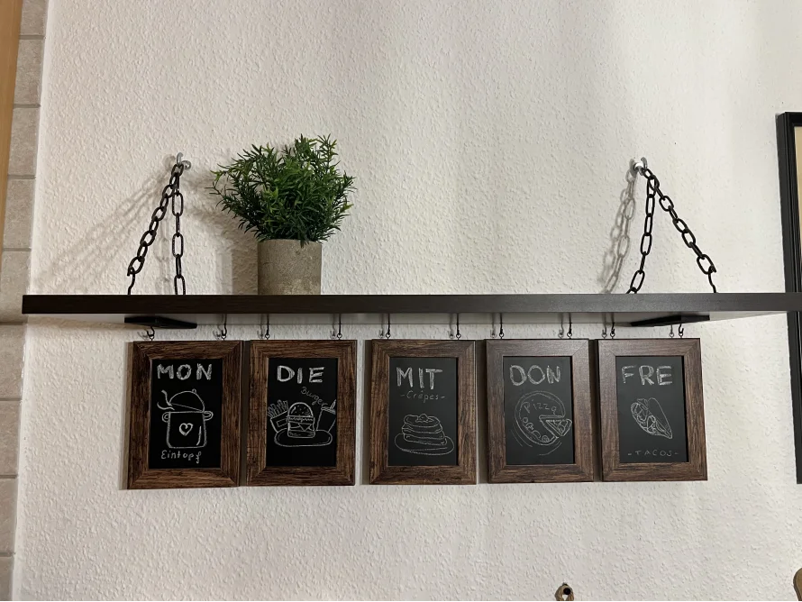 Wandregal mit Wochenplan aus Kreidetafeln und einer Pflanze