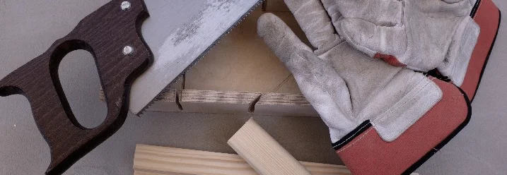 Handsäge, Holzbrett und Arbeitshandschuhe