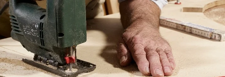 Person sägt Holzplatte mit Stichsäge