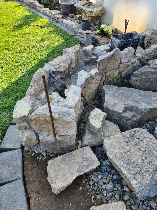 Bau einer Steinmauer im Garten mit einer Handschaufel und diversen Werkzeugen.