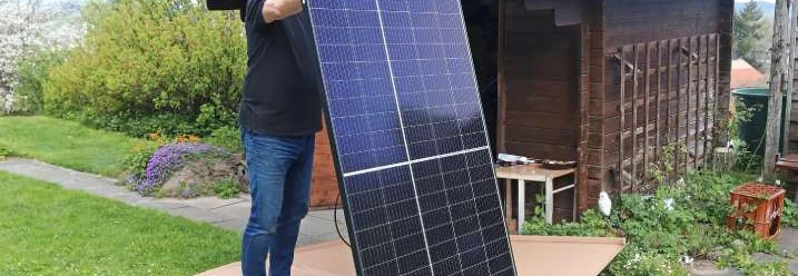 Eine Person hält ein Solarpanel vor einem Gartenhaus aus Holz.