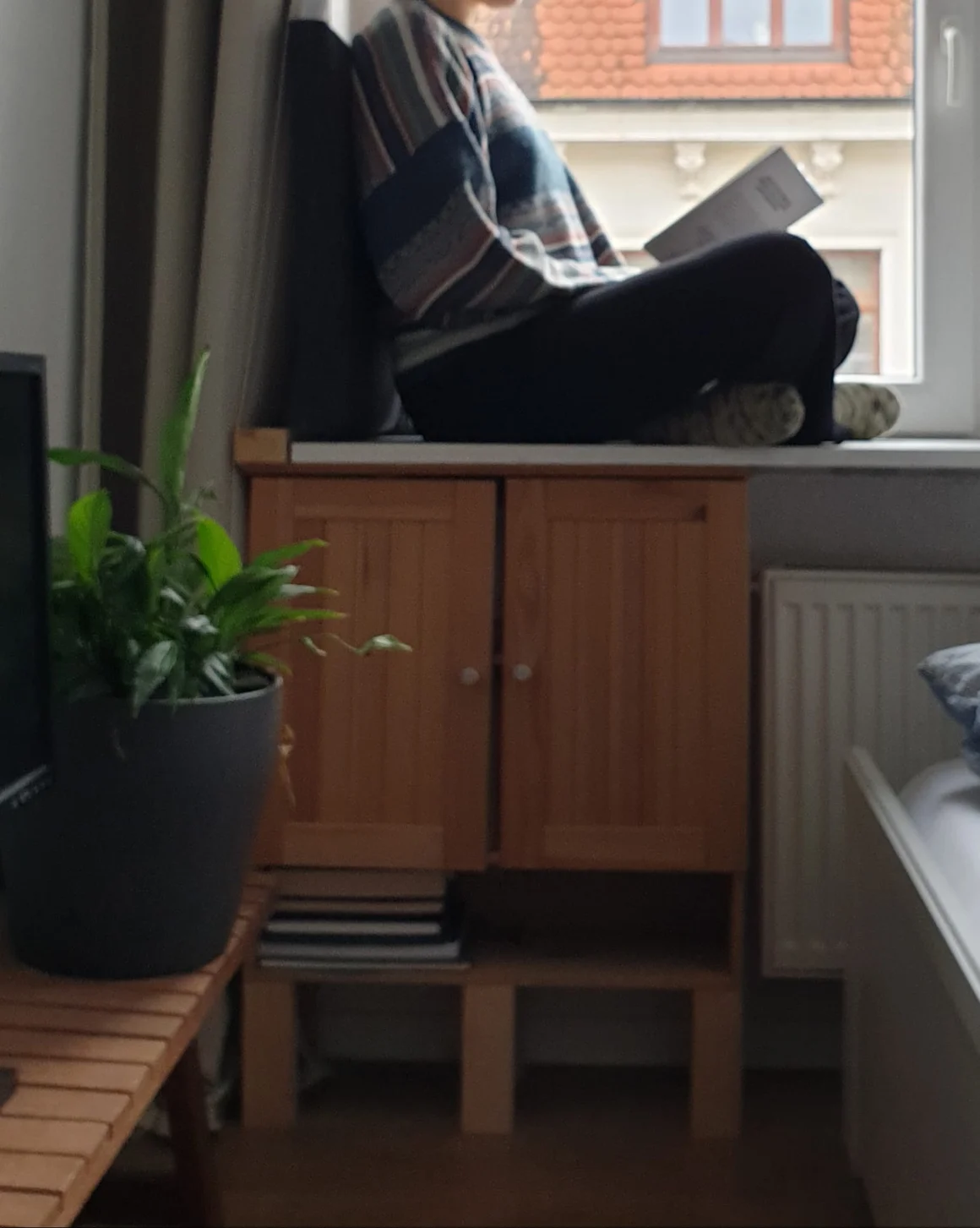 Eine Person sitzt auf der Fensterbank und liest ein Buch.