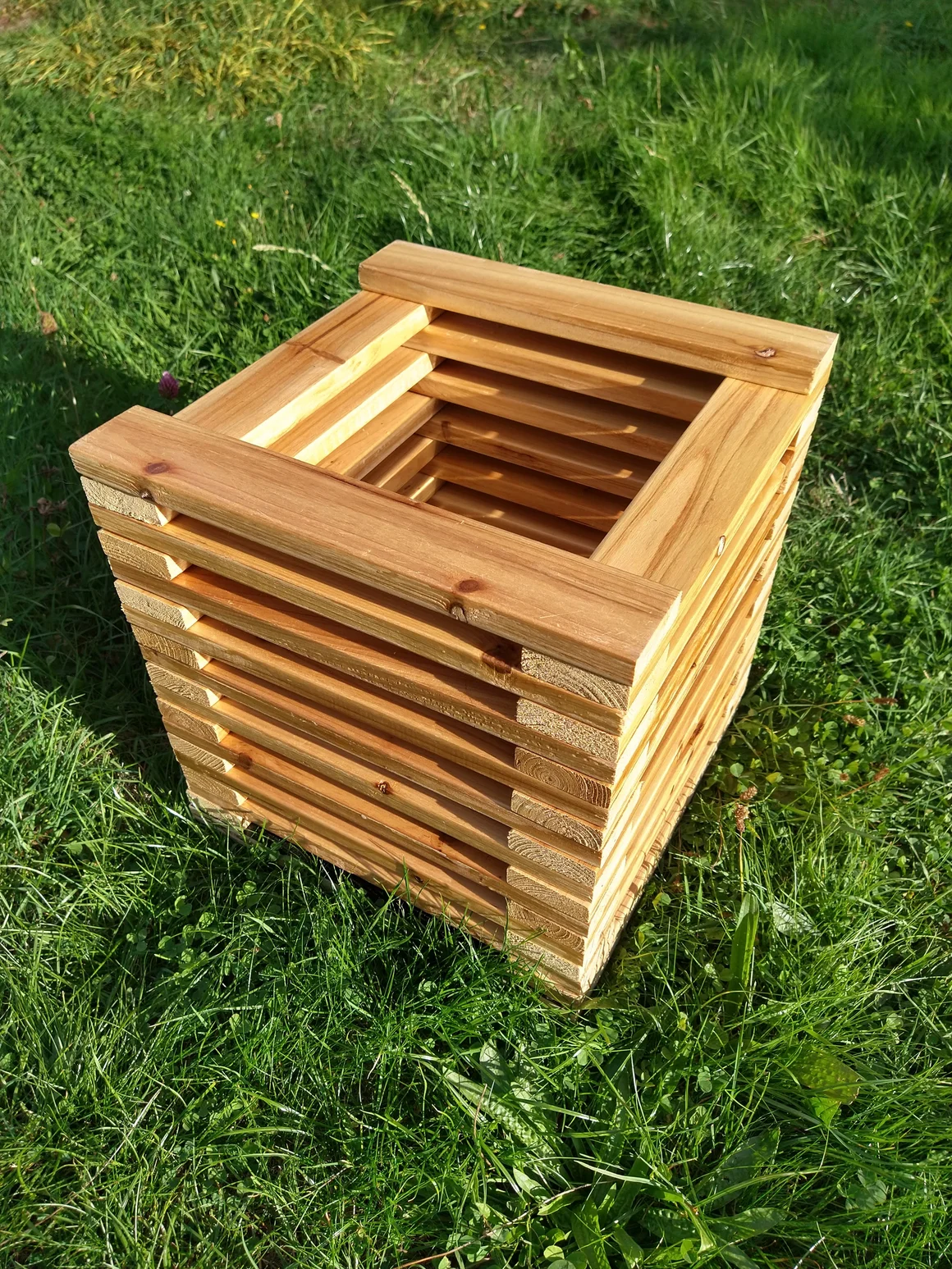 Ein würfelförmiger Pflanzkasten aus Holz auf einer Wiese.