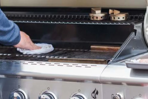 Person reinigt Gasgrill mit Tuch.