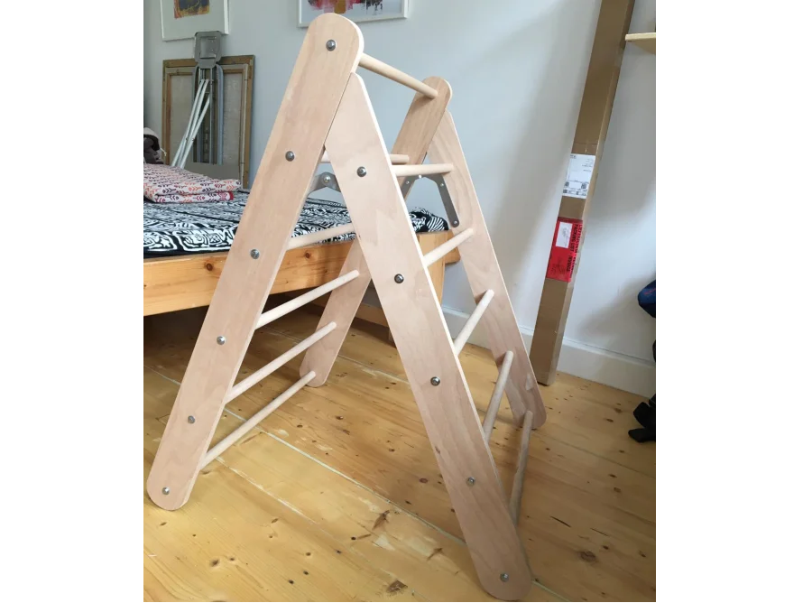 Ein Kletterdreieck aus Holz steht auf einem Holzboden in einem Zimmer.