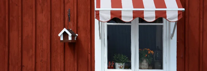 Ein Fenster an einer Holzwand mit einer rot-weißen Markise