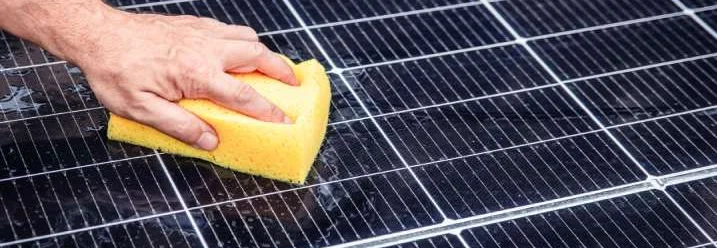 Person reinigt Solarpanel mit Schwamm