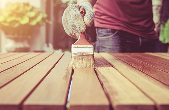 Person streicht Holztisch mit Pinsel.