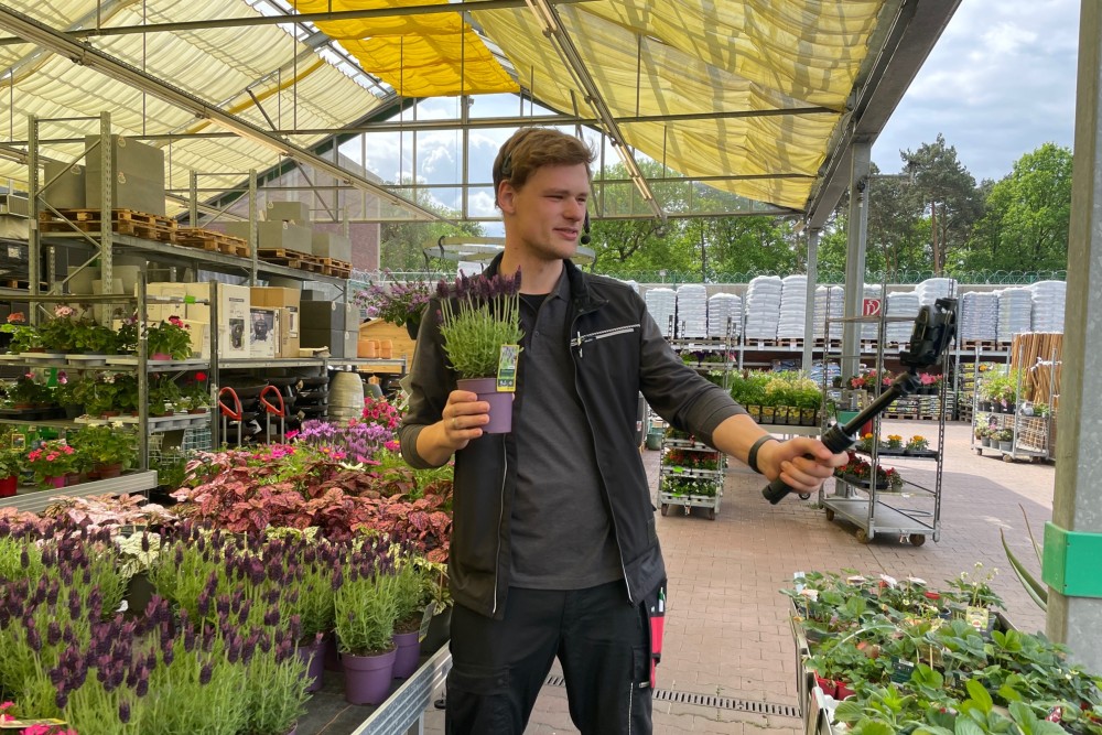 Eine Person in toom Arbeitskleidung filmt sich in einem toom Gartencenter